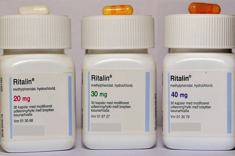 Ritalin medication containers labelled with different milligram strengths, with several tablets placed beside them on a clean surface.